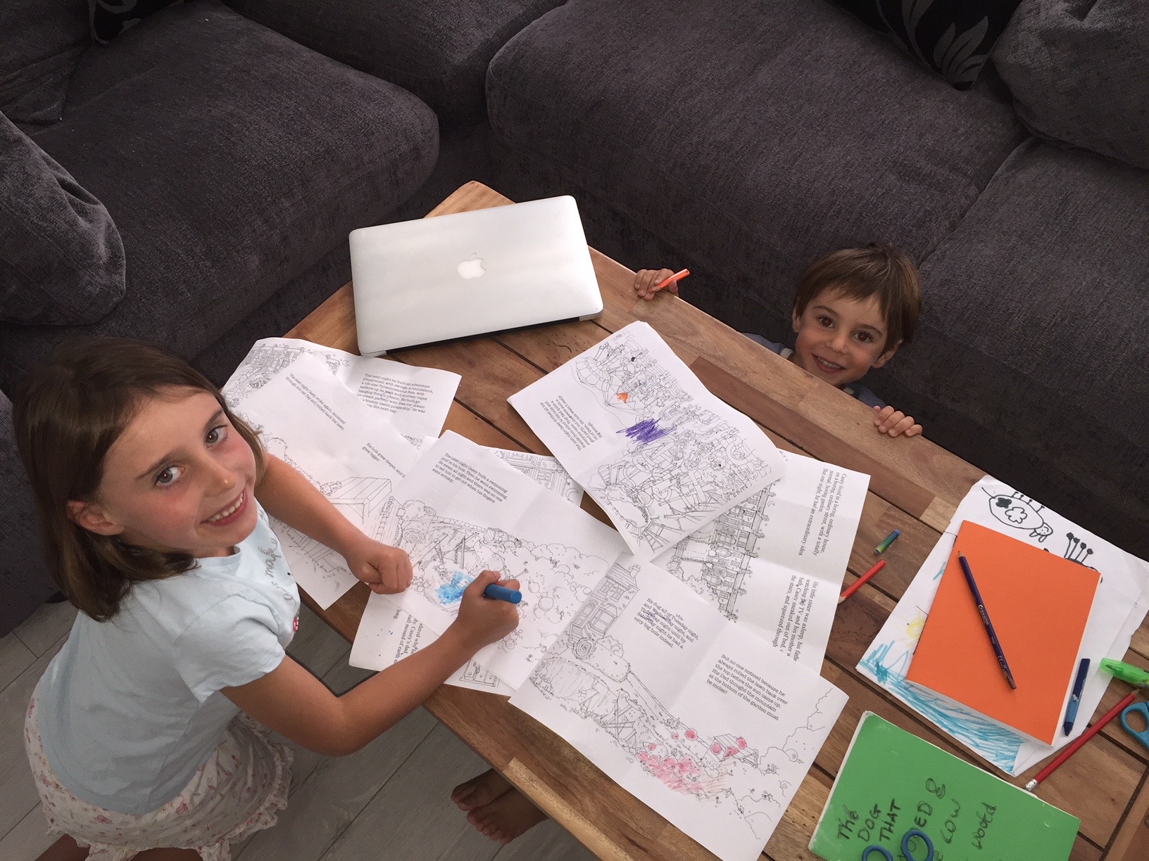 Alba and Rafa at a coffee table, colouring in printed rough sketches of the book with felt-tip pens, the family laptop open beside them.